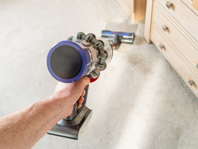 A picture of a hand holding a dyson vacuum cleaning a white carpet