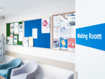 A blue sign with white writing saying waiting room in an NHS setting