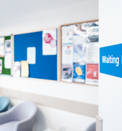 A blue sign with white writing saying waiting room in an NHS setting