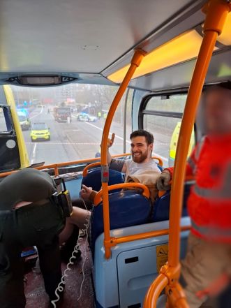 Gideon Ingram on smiling and giving a thumbs up on the bus, with emergency staff