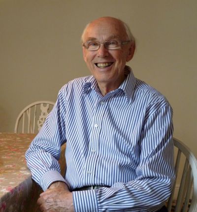 A gentleman in a blue stripy shirt smiling at his breakfast table