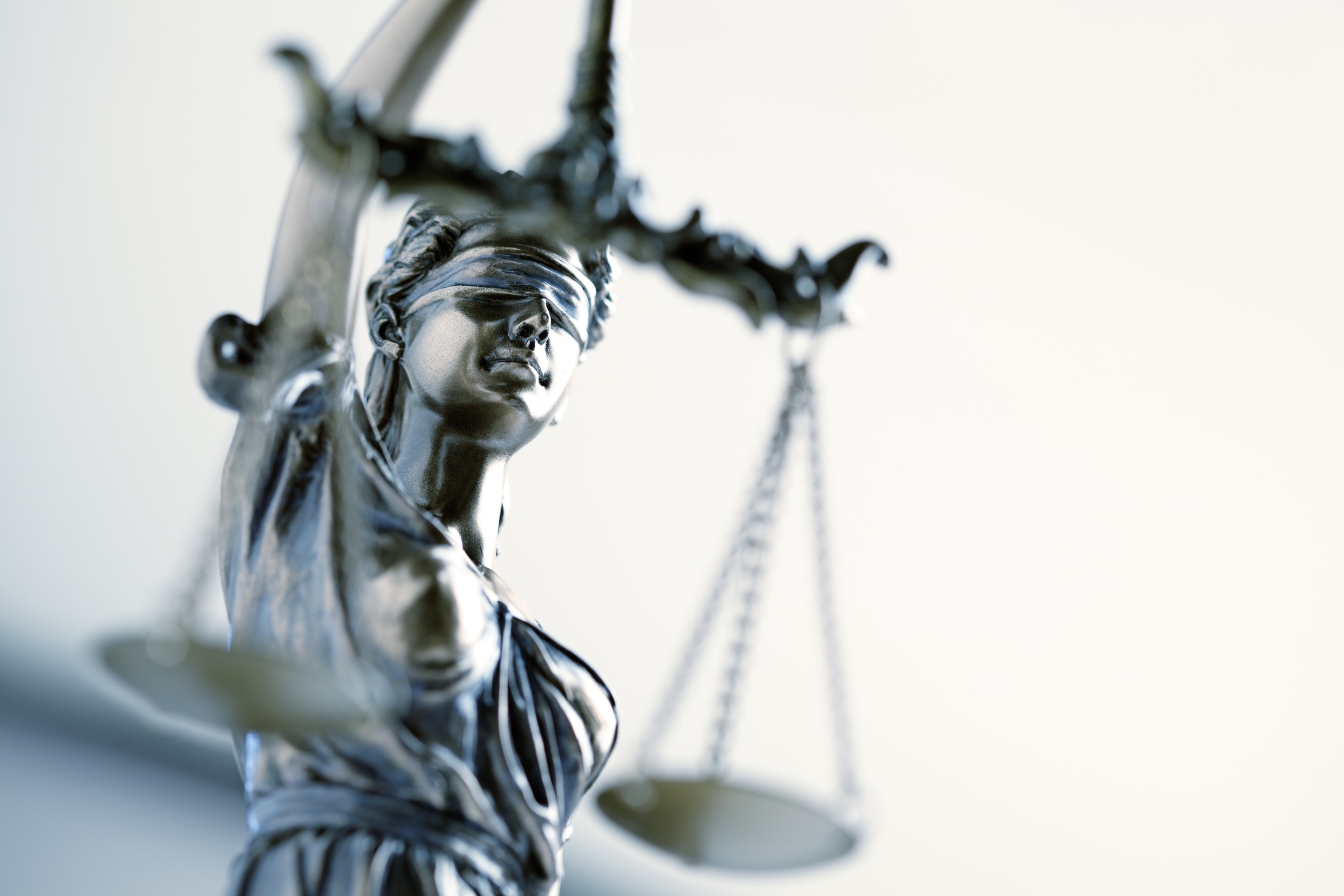 Close-up photograph of a metallic Lady Justice statue wearing a blindfold and holding balanced scales.