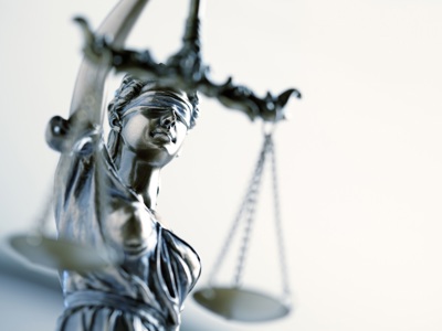 Close-up photograph of a metallic Lady Justice statue wearing a blindfold and holding balanced scales.