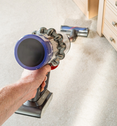 A picture of a hand holding a dyson vacuum cleaning a white carpet