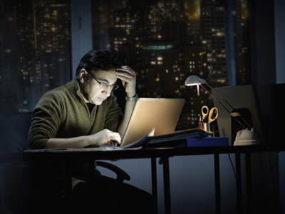 Man, sat in the dark, working on laptop
