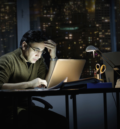 Man, sat in the dark, working on laptop