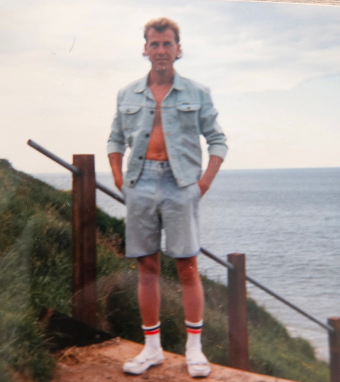 Picture of Paul Crossley standing in front of a grassy hill and the sea
