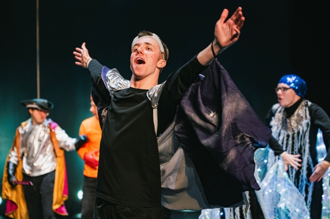 Danny Thomas performing on stage. He is wearing a black shirt and cape. 