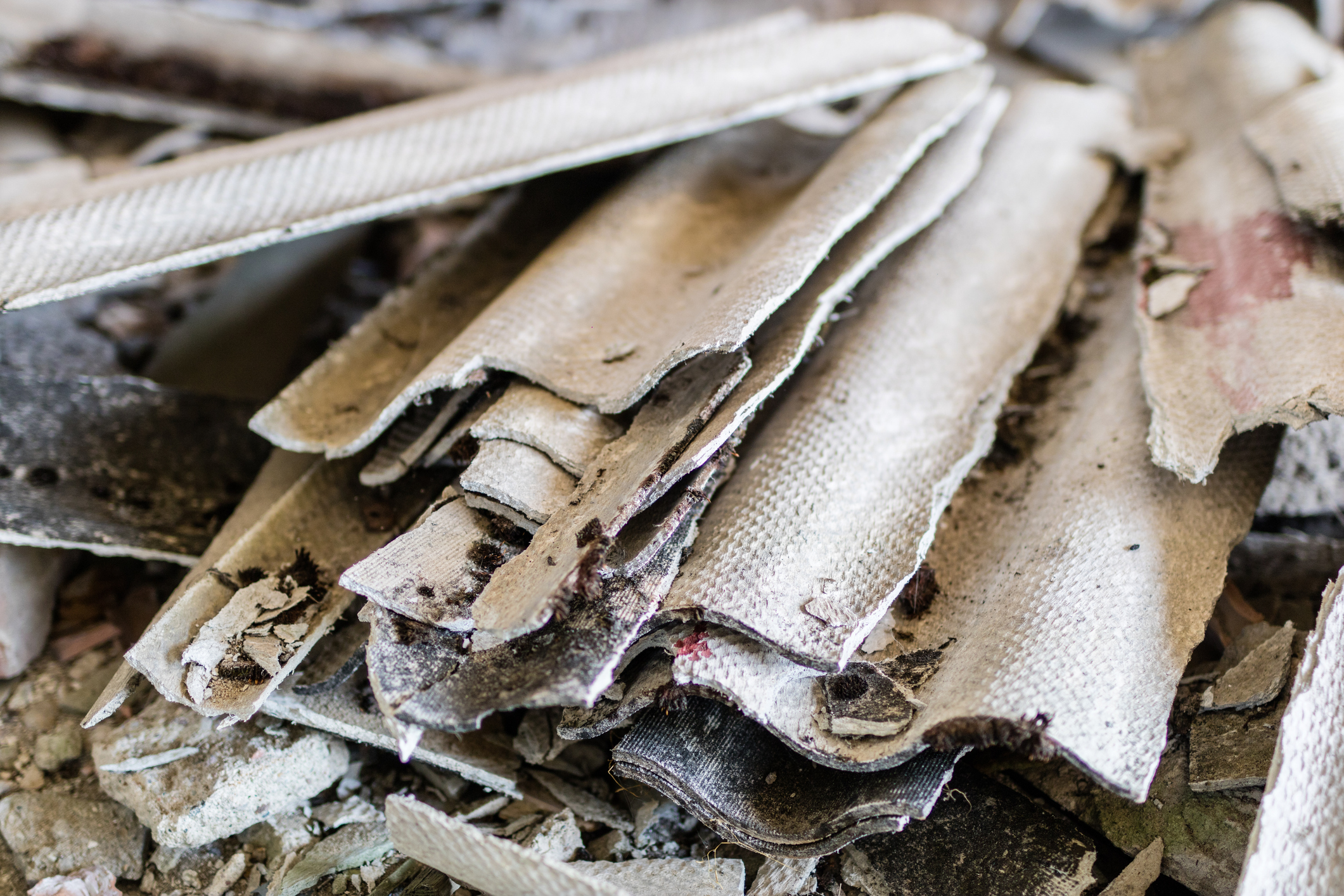 Close-up photograph of deteriorating corrugated asbestos cement sheets lying among rubble and dust