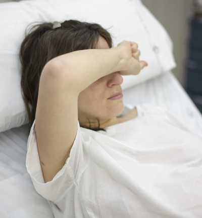A woman in a hospital bed with her arm over her face