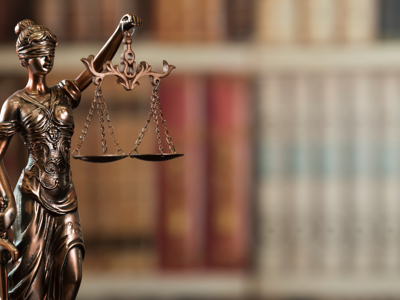 Bronze Lady Justice statue holding balanced scales, with blurred bookshelves in the background
