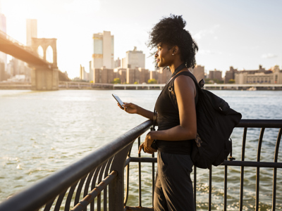 USA, New York City, Brooklyn, woman with cell phone standing at the waterfront