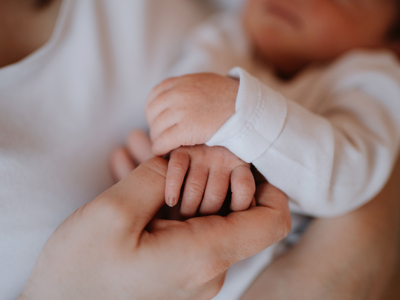 A mother gently holding a baby and touching the baby's hand
