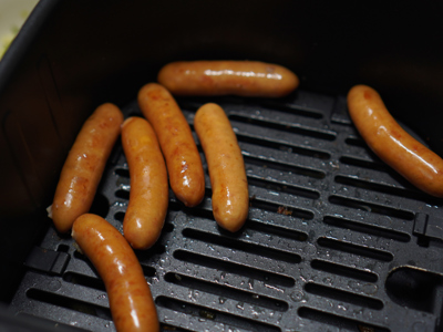 Seven brown sausages on a black metal air fryer griddle