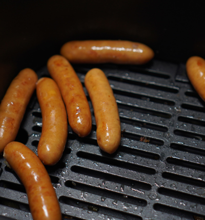 Seven brown sausages on a black metal air fryer griddle