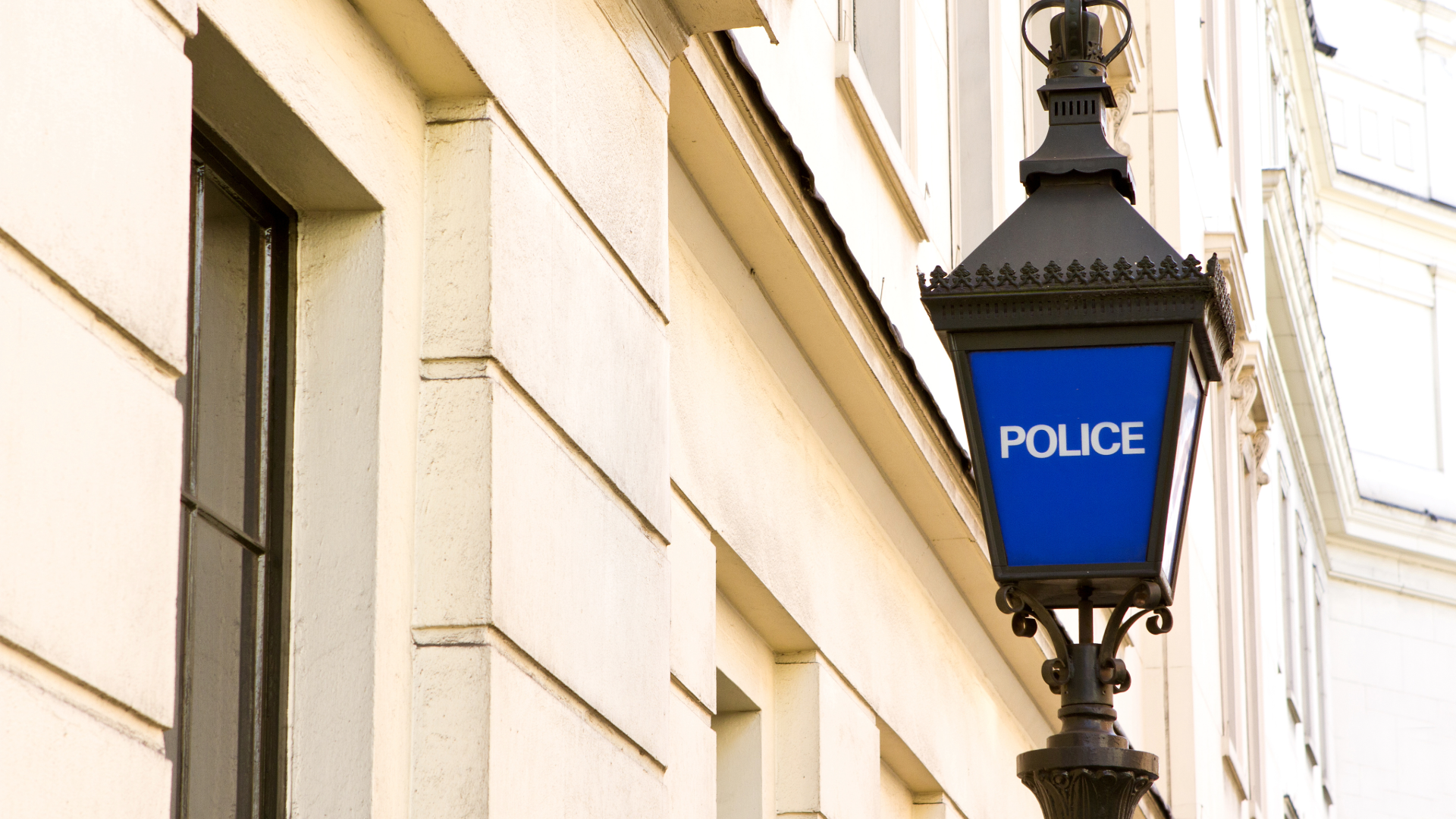 Blue police lantern sign mounted on the exterior wall of a light-coloured historic building