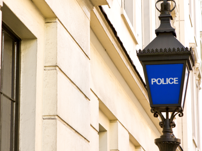 Blue police lantern sign mounted on the exterior wall of a light-coloured historic building