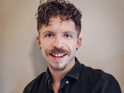 Adam Barber, Media Relations Manager, wearing a dark button-up shirt in a professional headshot against a plain background.