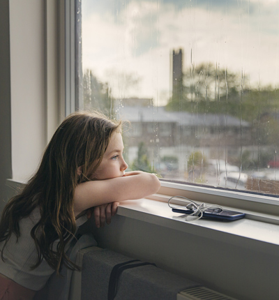 Young girl looking out of window on a rainy day